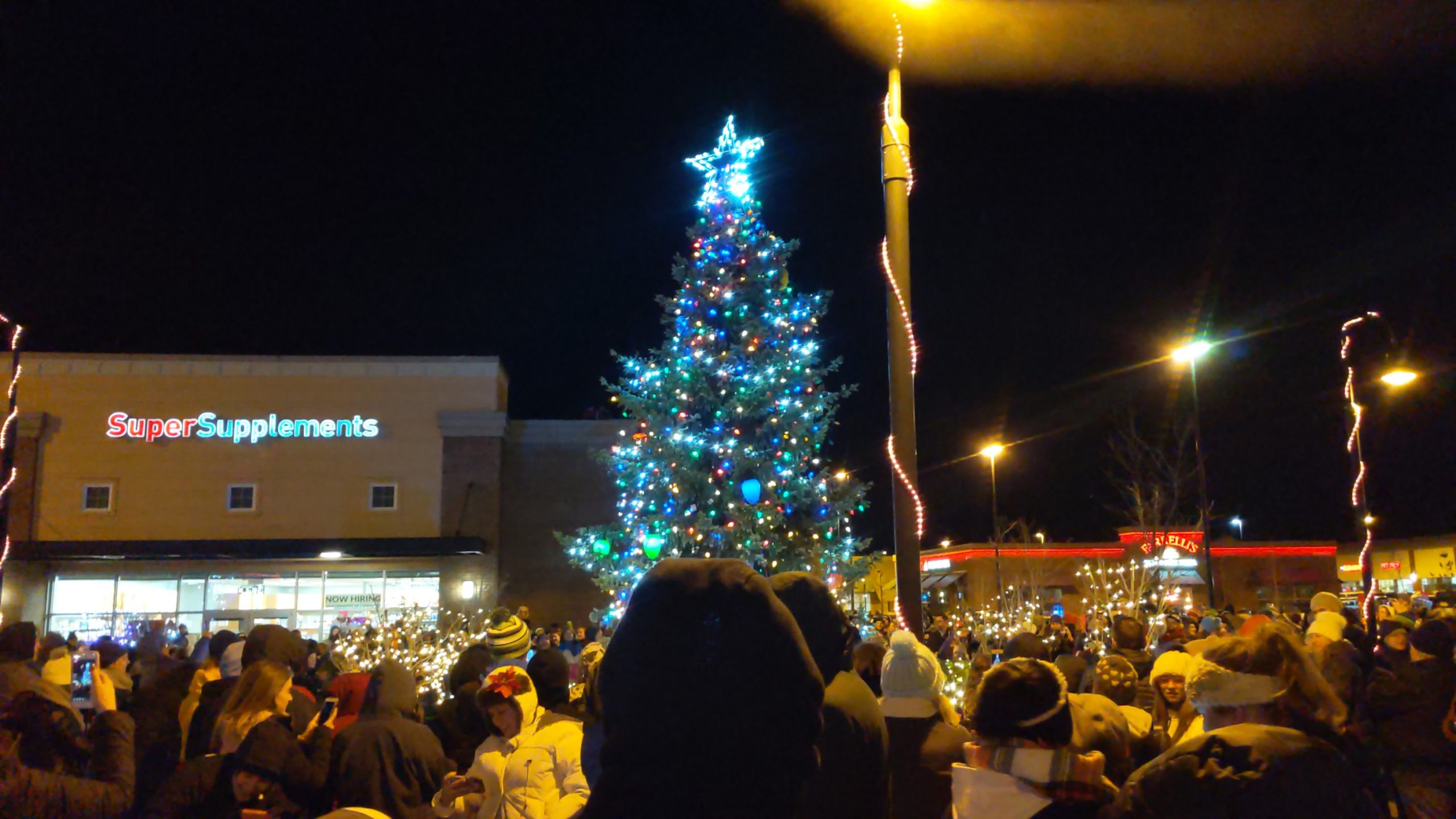 A photo of a lit Christmas tree in a square while a group of people look on.