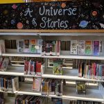 A shelf of children's books with a large sign that says "A universe of Stories" with pictures of planets and stars.